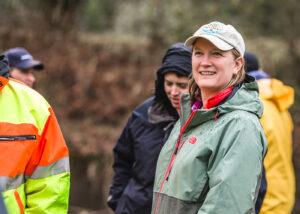 A clean water services employee stands in a tree for all hat while outside in the rain.