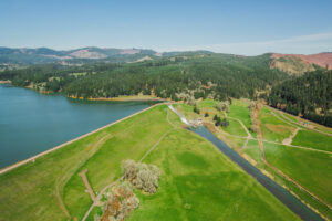 An aerial view of where water is released from Scoggins Dam. Part of Hagg Lake is visible on the left, with trees and hills in the background.