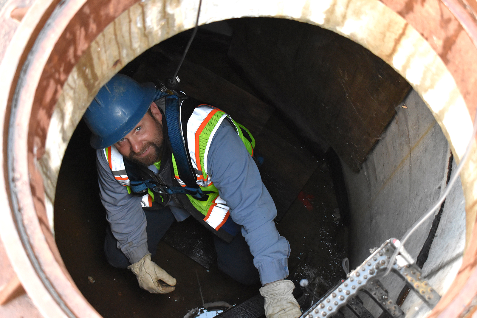 A Clean Water Services Employee Smiles from within a man hole.