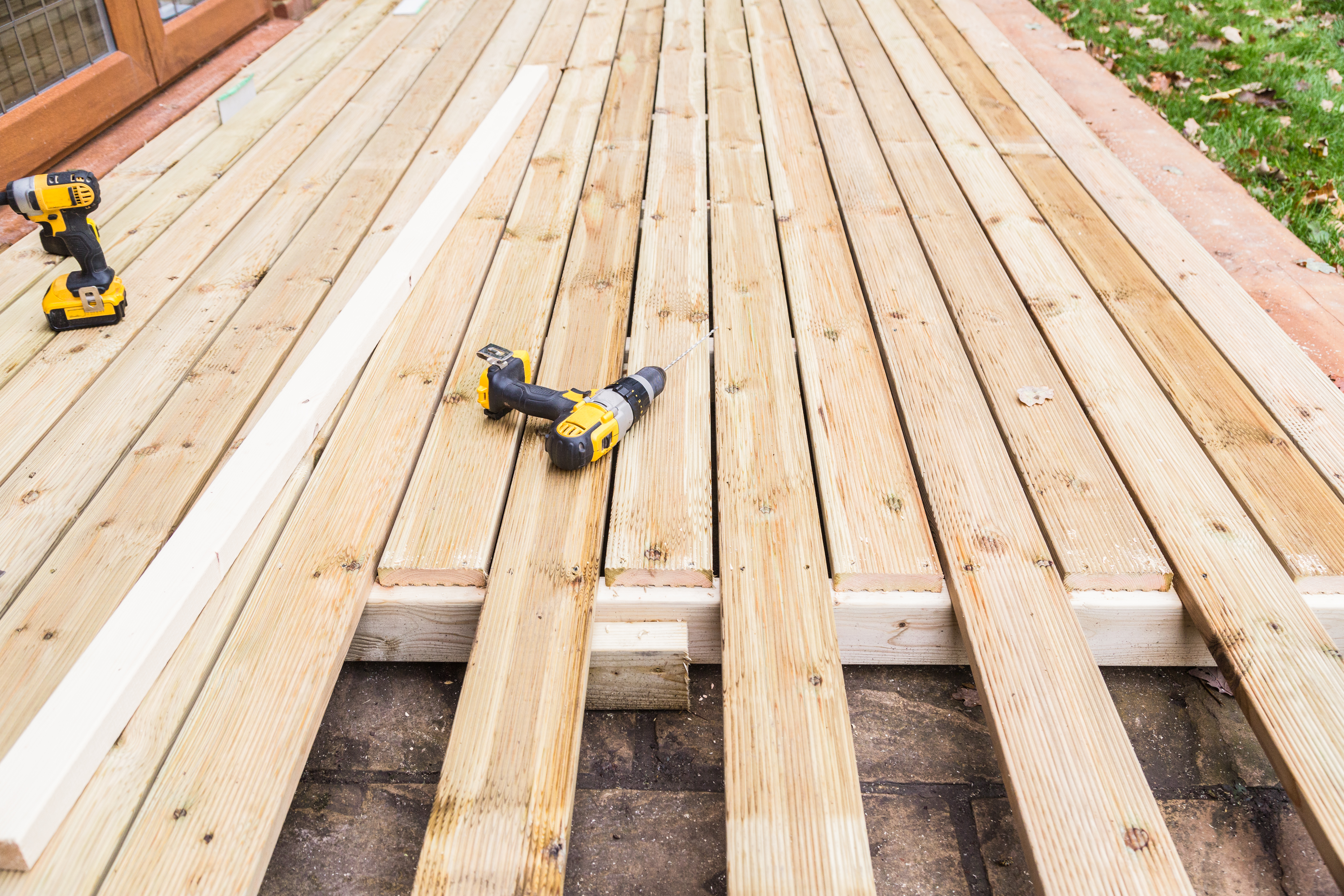 A new wooden, timber deck being constructed. it is partially completed. two drill can be seen on the decking.