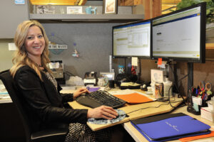 A Clean water services employee works on her computer in the cubical at the office and smiles at the camera