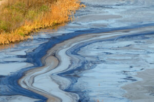 Hazardous waste in a natural area floating within the water. large waste swirls line the top of the water.