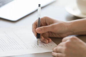 A person's hands signing document with a black ink pen
