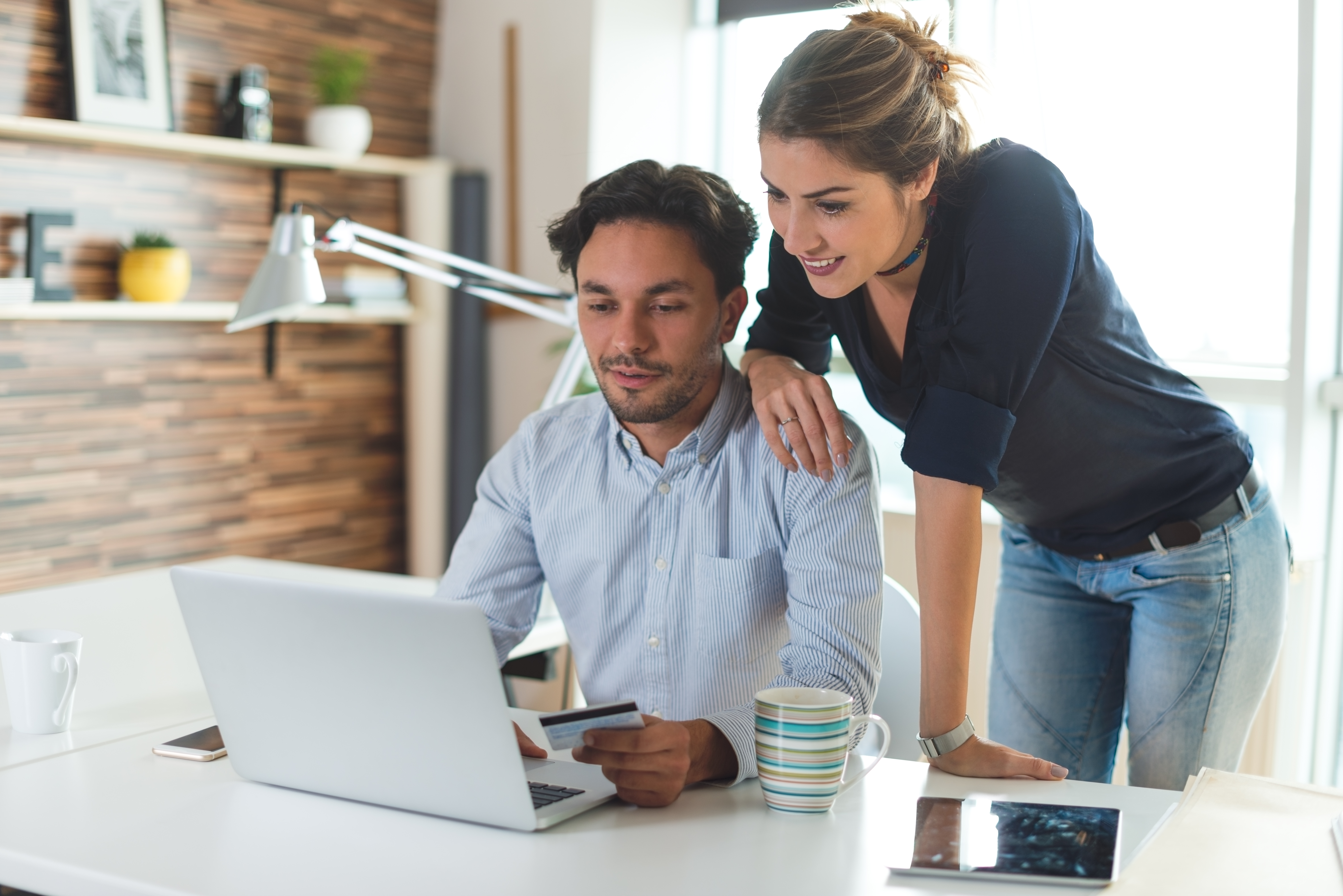 Two customers, one sitting on the computer, the other looking over his shoulder, looking at a computer while in the comfort of their home. They enter credit card information to pay their water bill from home.
