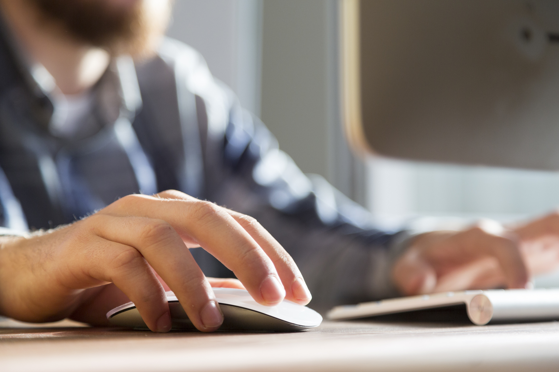 Man working on a computer, his right hand sits on the computer mouse while the other rests on the keyboard while typing