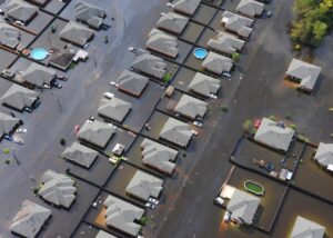 An Aerial image of a residential area completely flooded, leaving everything but the rooftops, trees, and cars underwater.