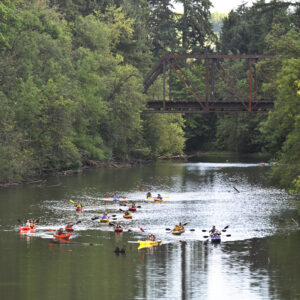 Current view of the Tualatin River with about a dozen folks paddling on the water.