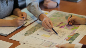 Planning document with multiple hands displayed including one pointing to the paper.