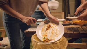 Person scraping a white plate with food into a lined garbage can
