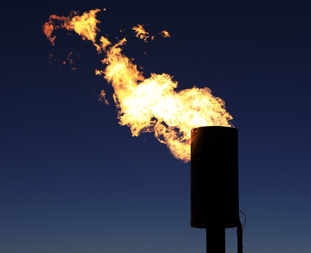 A flame burns excess methane out of a digester, against a night sky.